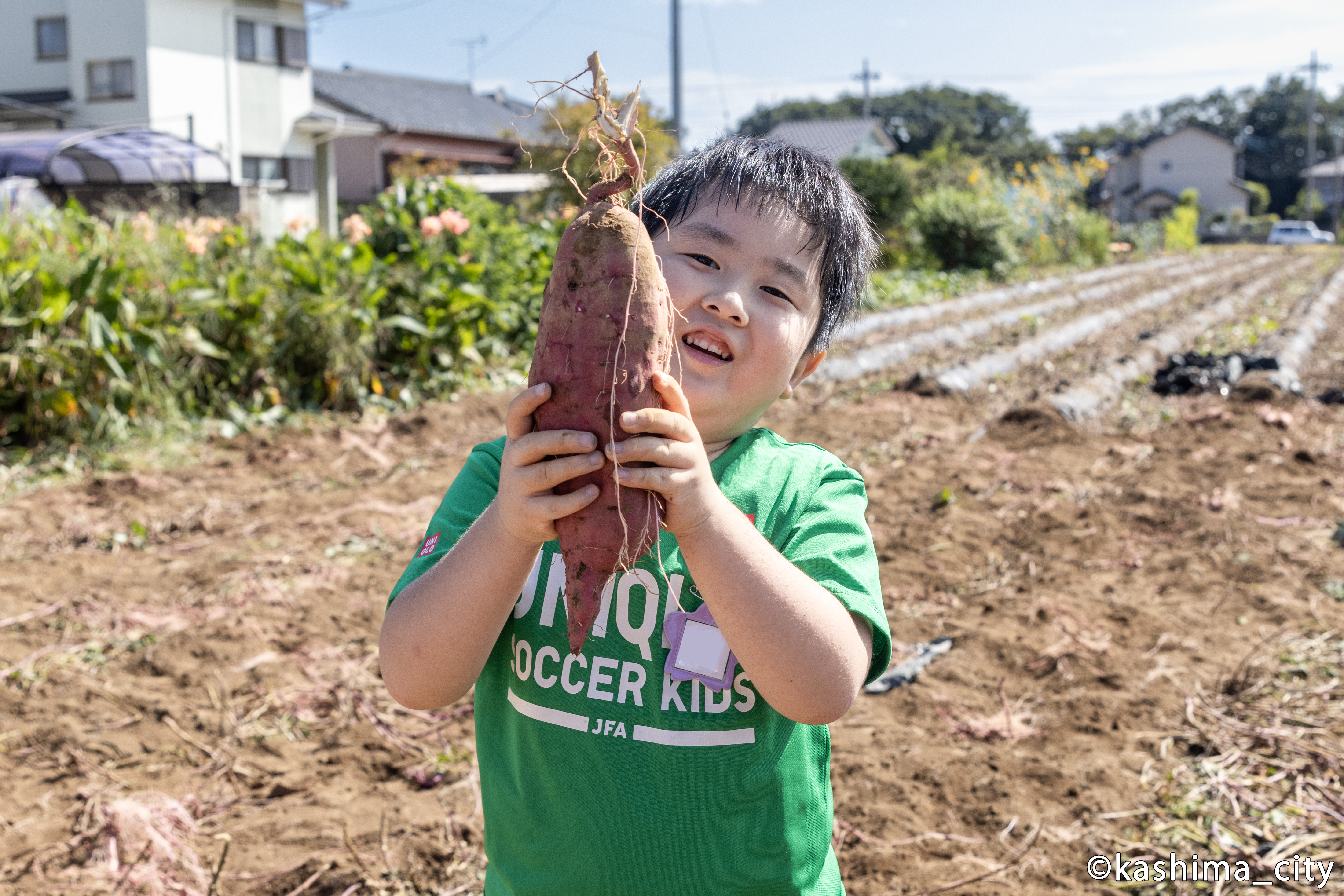 大きなサツマイモを顔の前に掲げる様子