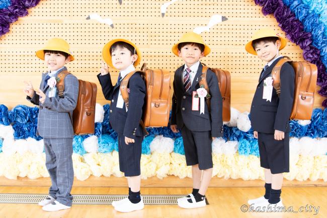 男子児童4人がランドセルと黄色い帽子を身に着けて記念撮影する様子